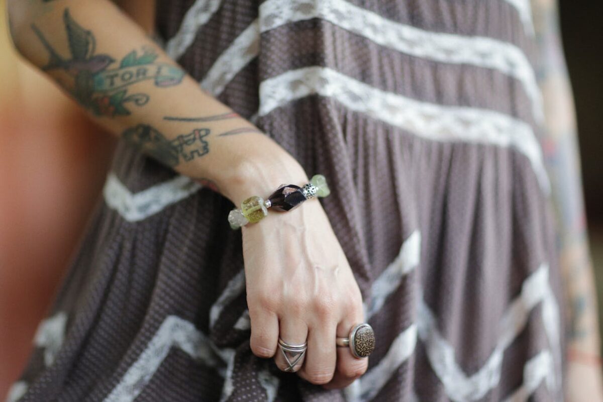 Close-up of a tattooed arm wearing gemstone rings and a bracelet on a patterned dress.