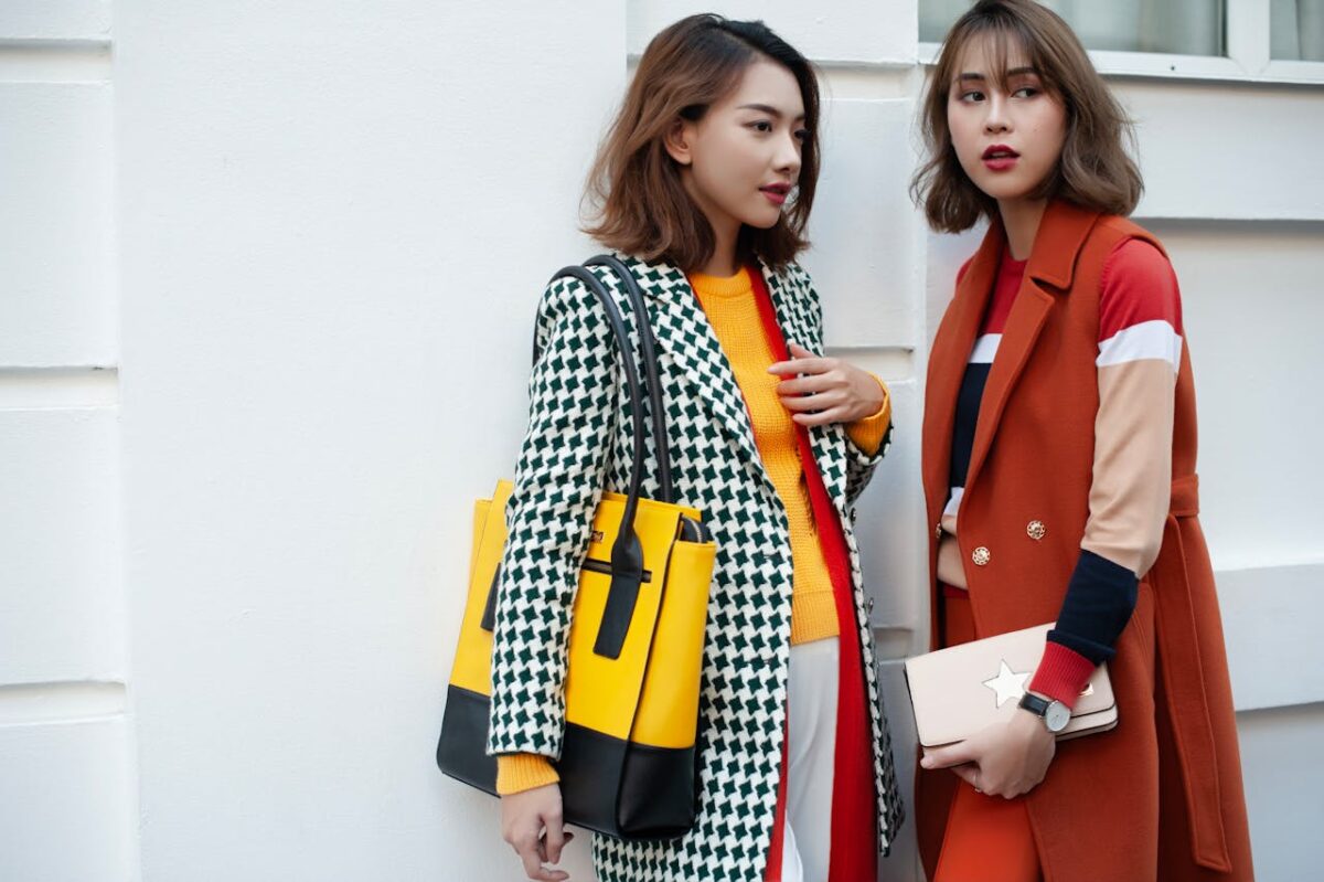 Service Two fashionable women in vibrant winter attire posing outdoors, showcasing chic handbags and coats.