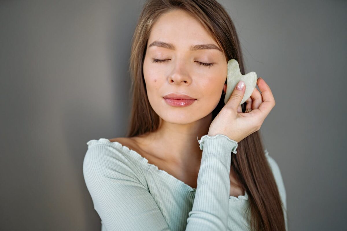 Young woman enjoying a relaxing gua sha facial massage with eyes closed, focusing on skincare routine.